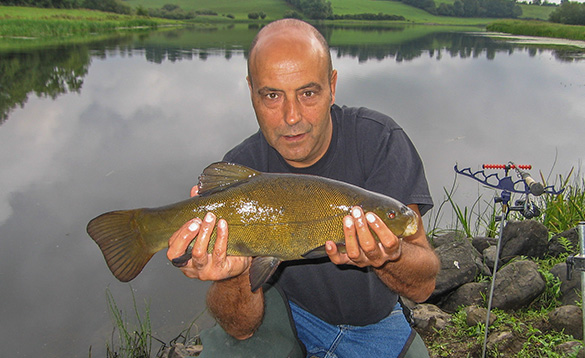 angler knelt at the edge of a river holding a tench/