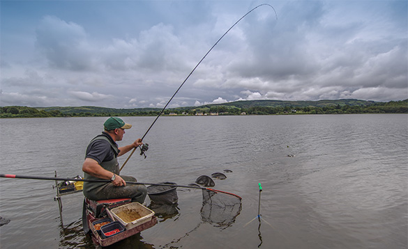 angler sitting on a tackle box in the shallow waters at the edge of a river fishing/